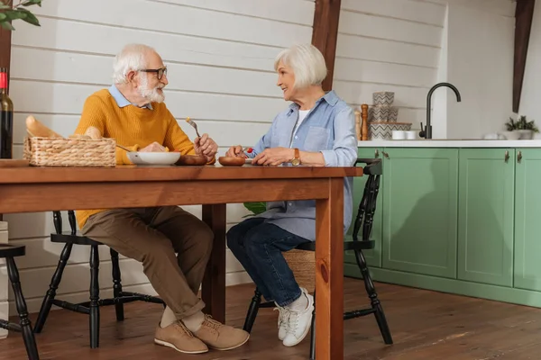 Piena lunghezza di felice coppia anziana guardando l'un l'altro mentre si mangia cena vegetariana a tavola in cucina — Foto stock