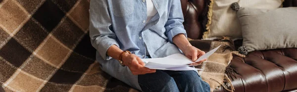 Cropped view of elderly woman holding bills while sitting on couch at home, banner — Stock Photo