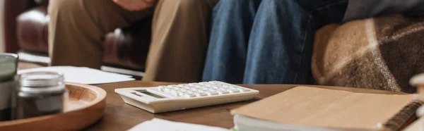 Cropped view of elderly couple sitting near table with white calculator at home on blurred background, banner — Stock Photo