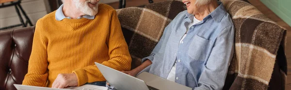 Vue recadrée du couple âgé avec journal et ordinateur portable sur le canapé à la maison, bannière — Photo de stock