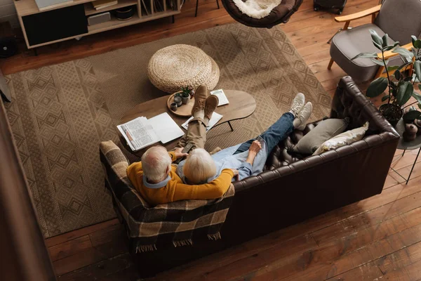 Blick aus der Vogelperspektive auf ein älteres Paar, das sich beim Fernsehen auf der Couch im Wohnzimmer umarmt — Stockfoto