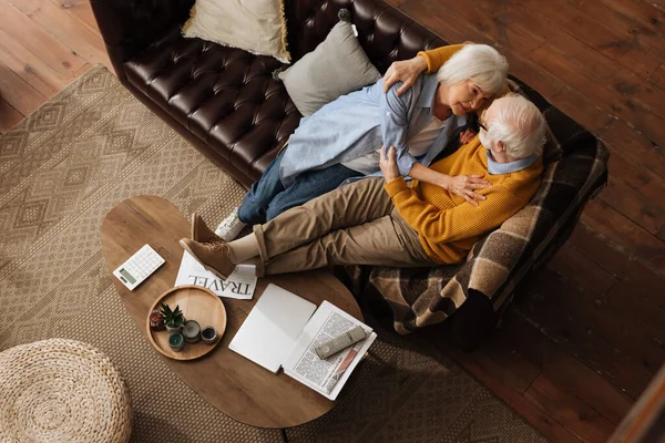Vista superior de feliz casal de idosos olhando uns para os outros, enquanto abraçando no sofá em casa — Fotografia de Stock
