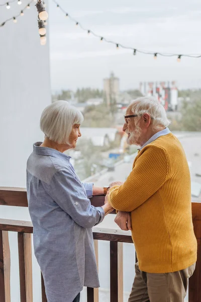 Smiling senior husband holding hands with wife on terrace on blurred background — Stock Photo