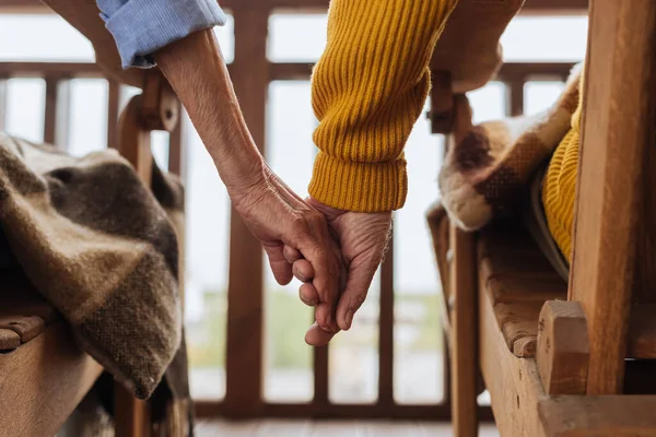 Cropped view of elderly couple holding hands on terrace on blurred background — Stock Photo