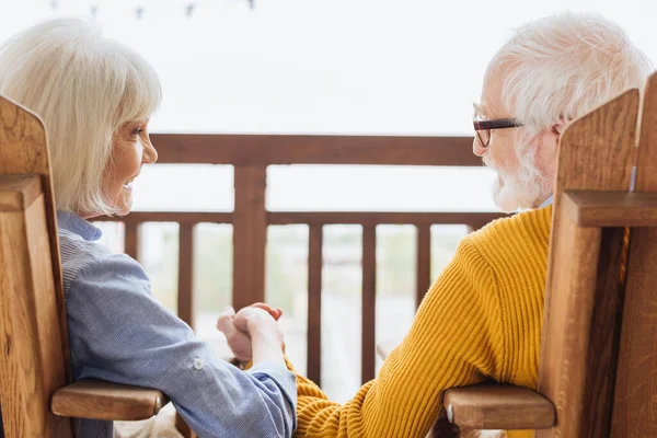 Glückliche Seniorin lacht, während sie auf der Terrasse vor verschwommenem Hintergrund Händchen hält — Stockfoto