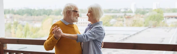 Feliz pareja de ancianos mirándose mientras bailan en la terraza sobre fondo borroso, pancarta - foto de stock