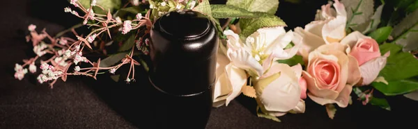 Rose bouquet and urn with ashes on black background, funeral concept, banner — Stock Photo