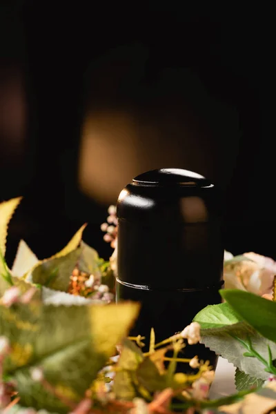 Bouquet and urn with ashes on black background, funeral concept — Stock Photo