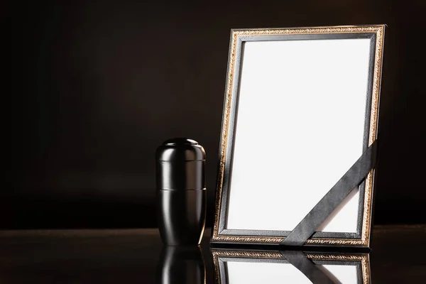 Urn with ashes, mirror with black ribbon on black background, funeral concept — Stock Photo