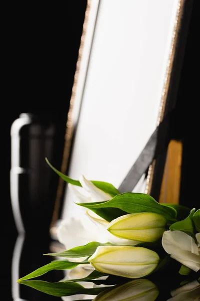 Flowers, mirror with black ribbon and urn with ashes, blurred background — Stock Photo