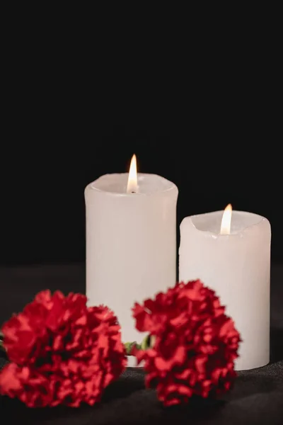 Rote Nelkenblumen und Kerzen auf schwarzem Hintergrund, Bestattungskonzept — Stockfoto
