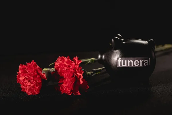 Flores de clavel rojo y alcancía sobre fondo negro, concepto de funeral - foto de stock