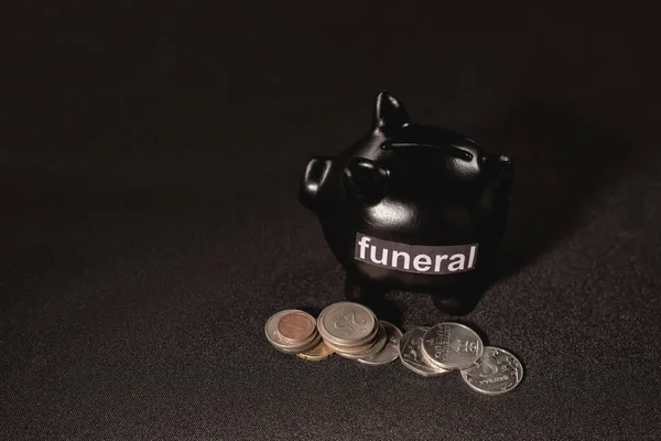 Salvadanaio con monete su sfondo nero, concetto funerario — Foto stock