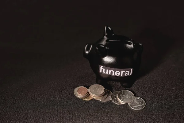 Piggy bank with coins on black background, funeral concept — Stock Photo