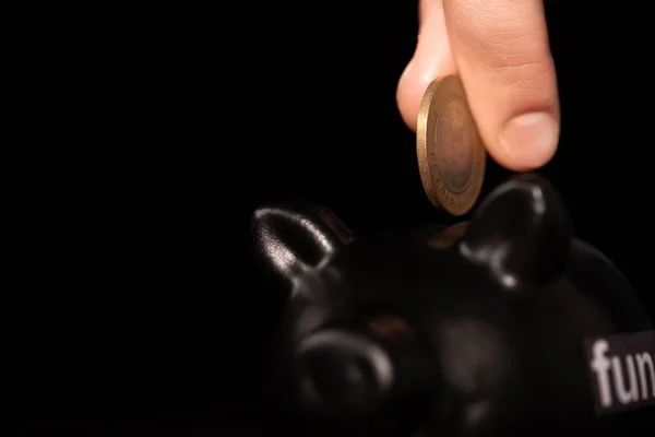 Vista recortada del hombre poniendo moneda en alcancía sobre fondo negro, concepto de funeral - foto de stock