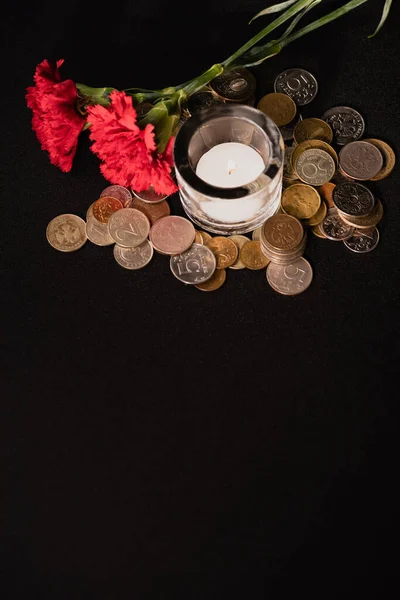 Claveles rojos, velas y monedas sobre fondo negro, concepto funerario - foto de stock