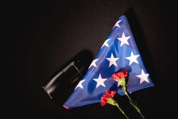 Vista superior de clavel rojo, cenizas y bandera americana sobre fondo negro, concepto funerario - foto de stock