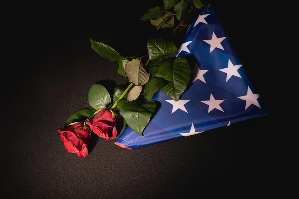 Vista superior de rosas rojas y bandera americana sobre fondo negro, concepto funerario - foto de stock