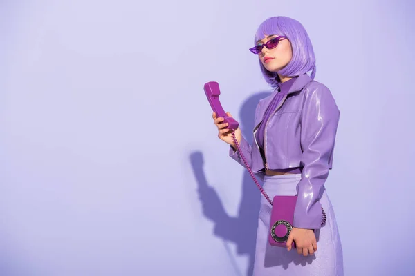 Young woman dressed in doll style with retro telephone on violet colorful background — Stock Photo