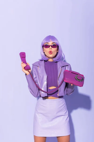 Shocked young woman dressed in doll style with retro telephone on violet colorful background — Stock Photo