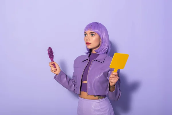 Young woman dressed in doll style with hair brush and mirror on violet colorful background — Stock Photo