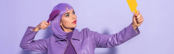 Jeune femme habillée de style poupée avec brosse à cheveux et miroir sur fond violet coloré, bannière — Photo de stock