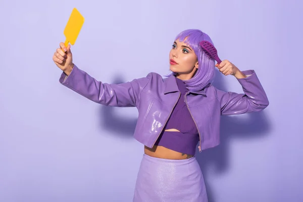 Junge Frau im Puppenstil mit Haarbürste und Spiegel auf violettem Hintergrund gekleidet — Stockfoto