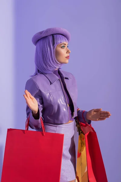 Junge Frau im Puppenstil mit roten Einkaufstaschen auf violett buntem Hintergrund — Stockfoto