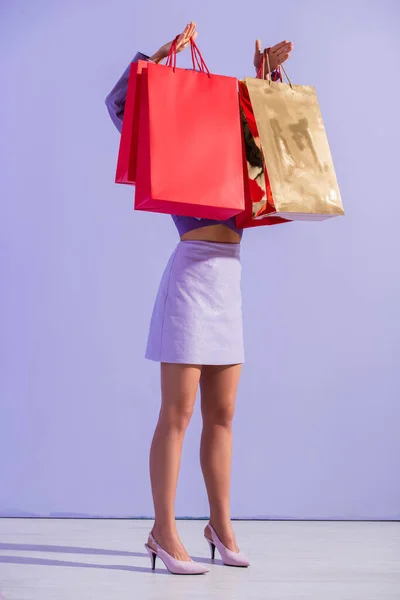 Young woman dressed in doll style with red shopping bags on violet colorful background — Stock Photo