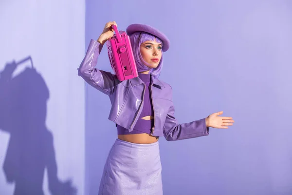 Young woman dressed in doll style posing with pink retro tape recorder on violet colorful background — Stock Photo