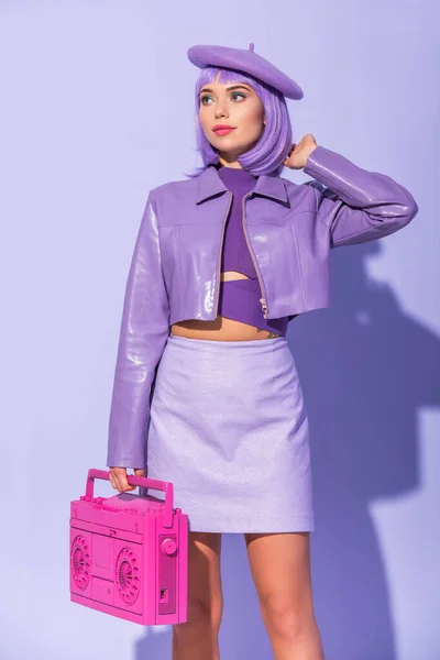 Молода жінка, одягнена в ляльковий стиль, позує з рожевим ретро магнітофоном на фіолетовому барвистому фоні — стокове фото