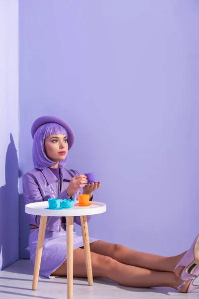 Jeune femme vêtue de style poupée en béret posant avec des plats de jouets sur fond violet coloré — Photo de stock