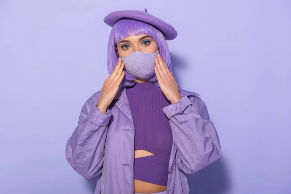 Jeune femme habillée de style poupée en masque médical et béret sur fond violet coloré — Photo de stock