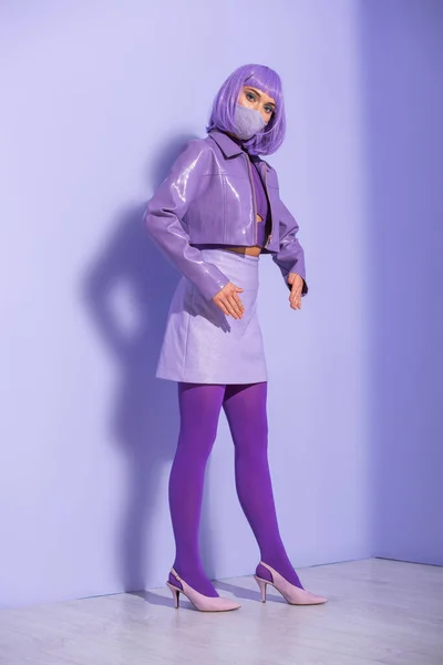 Jeune femme habillée de style poupée en masque médical sur fond violet coloré — Photo de stock