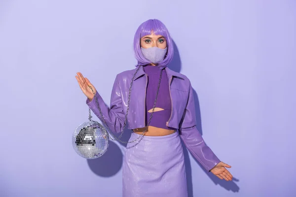Jeune femme habillée de style poupée en masque médical avec boule disco sur fond violet coloré — Photo de stock