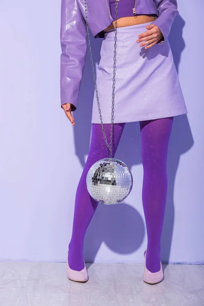 Vue recadrée de jeune femme vêtue de style poupée avec boule disco sur fond violet coloré — Photo de stock