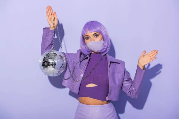 Giovane donna vestita in stile bambola in maschera medica con palla da discoteca su sfondo viola colorato — Foto stock