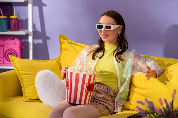 Smiling young woman posing as doll with popcorn in 3d glasses on yellow couch — Stock Photo