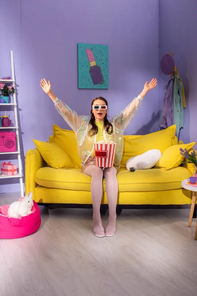 Young woman posing as doll with popcorn in 3d glasses on yellow couch — Stock Photo