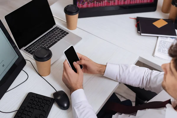 High angle view of smartphone with blank screen in hands of businessman on blurred foreground near computers and takeaway coffee — Stock Photo