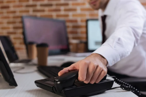 Vista recortada del hombre de negocios sosteniendo el teléfono cerca de las computadoras en un fondo borroso - foto de stock