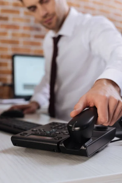 Cropped view of businessman on blurred background taking telephone handset — Stock Photo