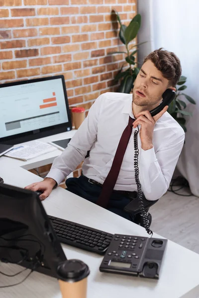 Homme d'affaires parlant au téléphone près des ordinateurs et du café pour aller au premier plan flou dans le bureau — Photo de stock