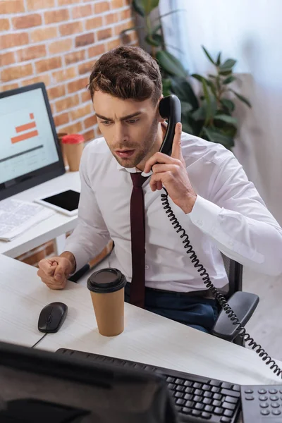 Uomo d'affari che parla al telefono vicino al caffè per andare e computer in primo piano sfocato — Foto stock