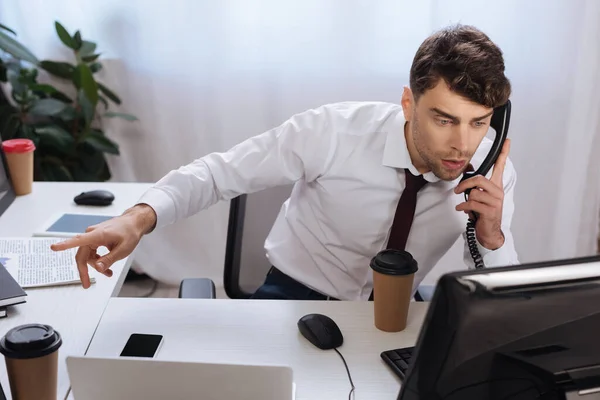 Бизнесмен разговаривает по телефону и показывает пальцем во время проверки финансовых курсов — стоковое фото