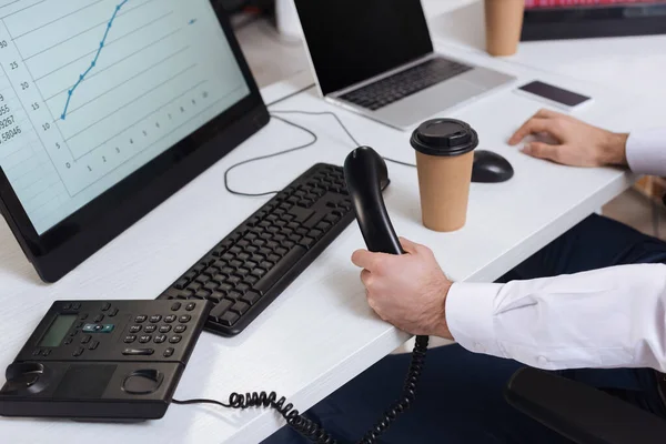 Vista ritagliata di uomo d'affari in possesso di telefono cellulare vicino take away caffè e computer su sfondo sfocato — Foto stock