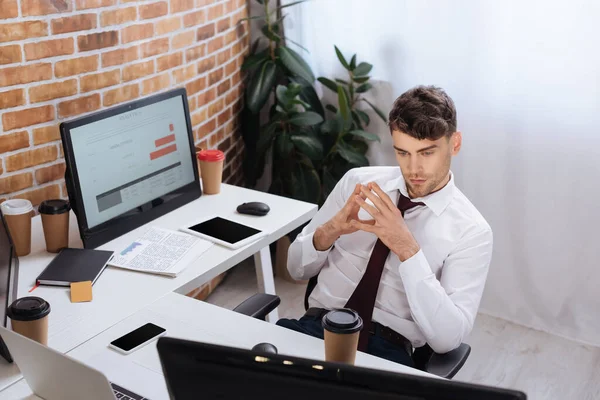Молодой бизнесмен смотрит на монитор компьютера возле кофе, чтобы пойти и гаджеты в офисе — стоковое фото