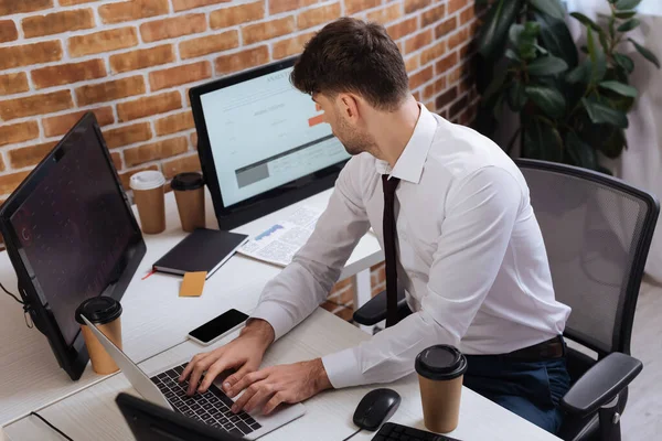 Homem de negócios usando laptop enquanto olha para o computador perto de tomar café no escritório — Fotografia de Stock