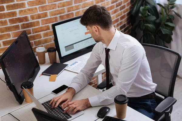 Businessman using laptop while looking at computer near takeaway coffee in office — Stock Photo