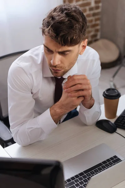 Homme d'affaires regardant l'ordinateur près de l'ordinateur portable et le café pour aller sur fond flou — Photo de stock